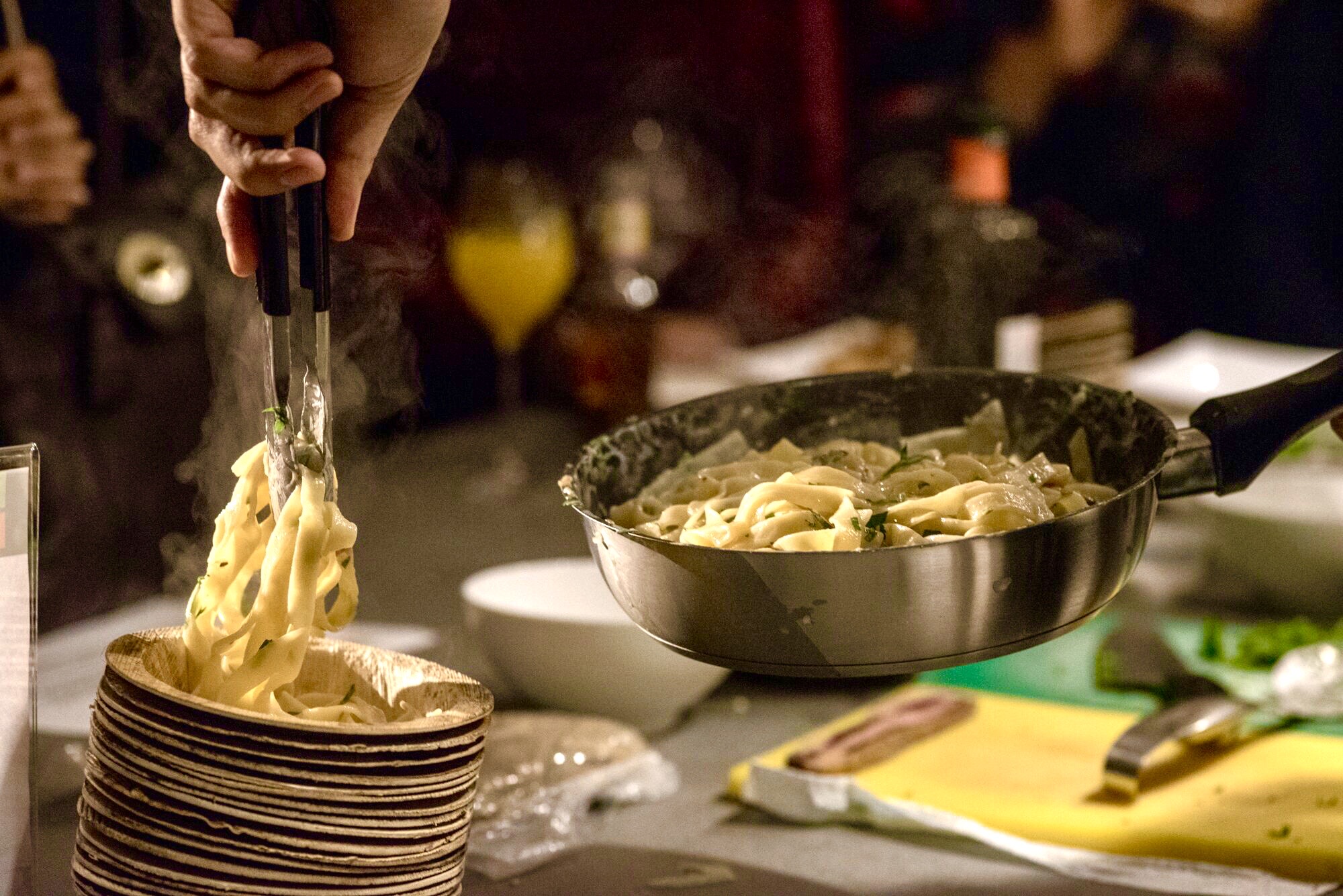 Hot pasta being served onto palm leaf plates at a catering event
